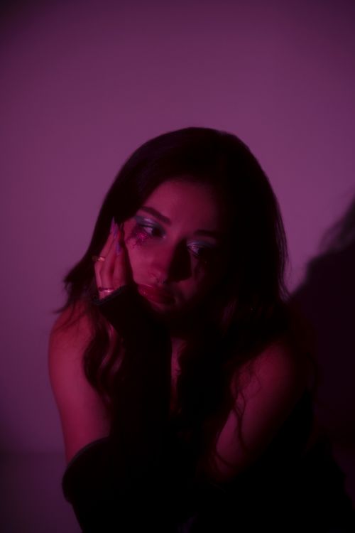Free A moody portrait featuring a woman with vibrant eye makeup against a soft purple studio backdrop. Stock Photo