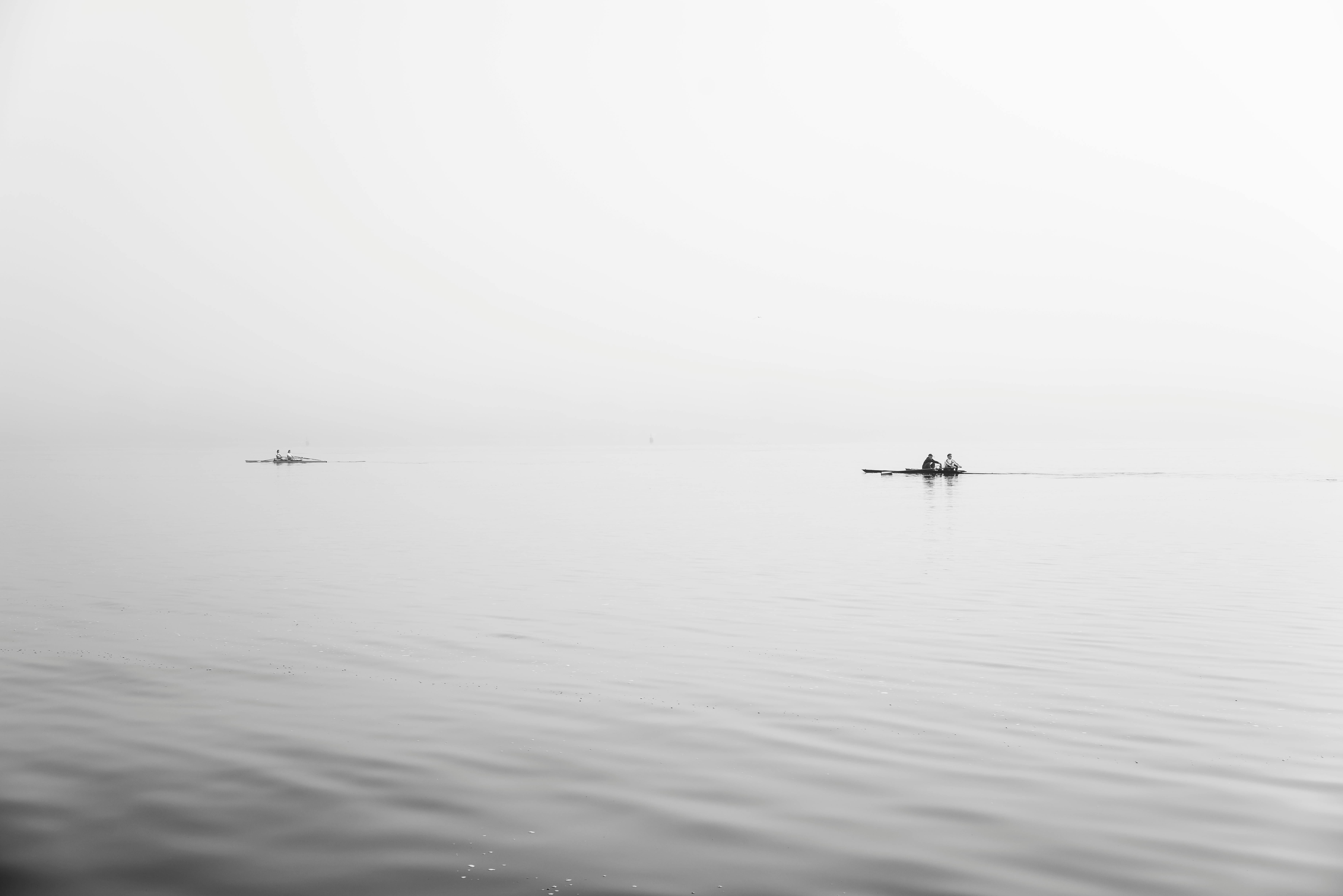 Peaceful black and white image featuring boats on calm water with a clear horizon, emphasizing serenity.