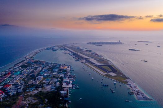 A stunning aerial view of a city with an airport runway by the ocean at twilight.