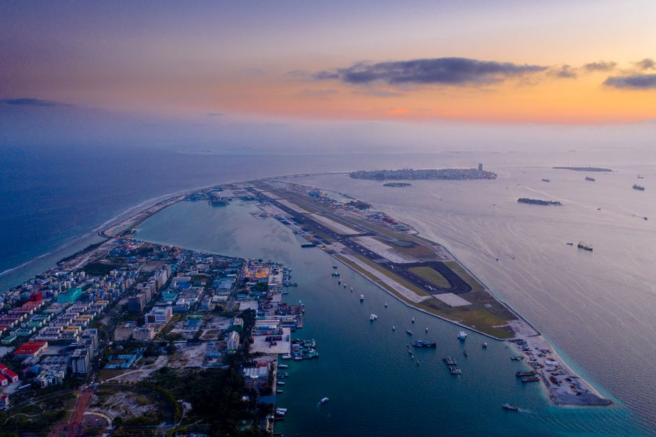 A stunning aerial view of a city with an airport runway by the ocean at twilight.