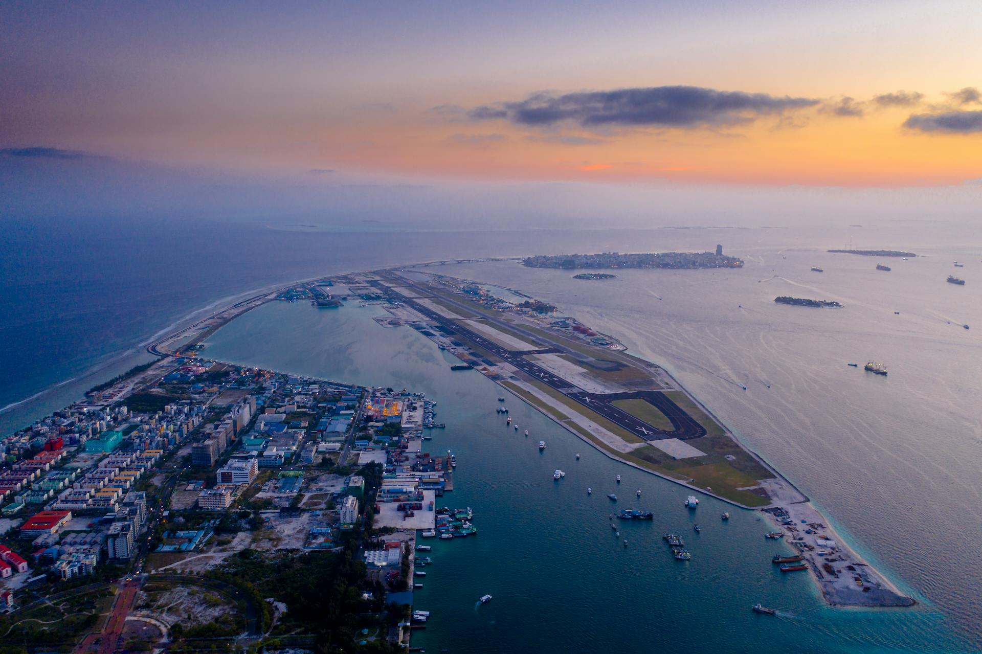 A stunning aerial view of a city with an airport runway by the ocean at twilight.