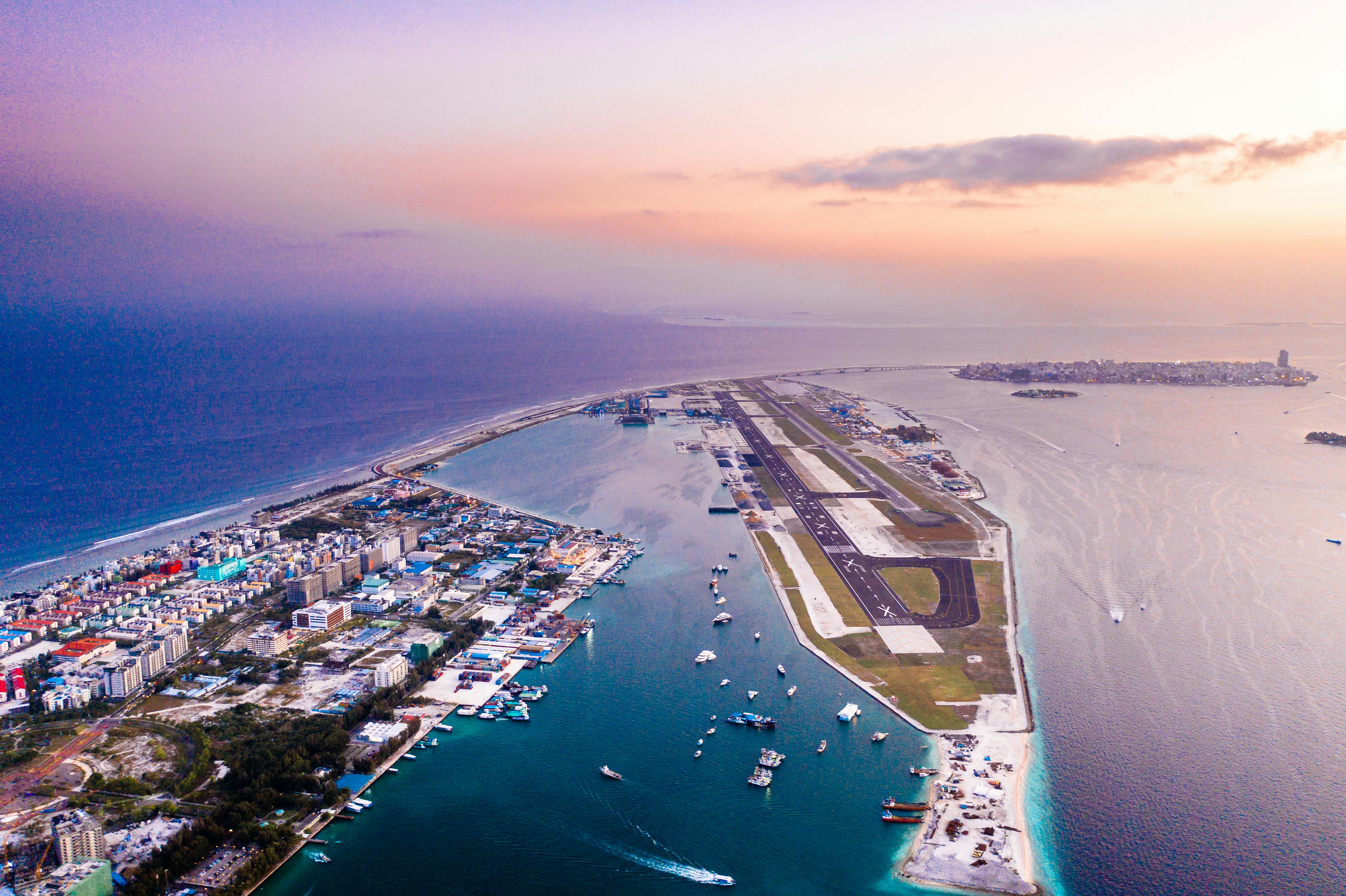 UAEThrive Daily News Roundup: A breathtaking aerial view of a coastal city and airport at sunset with vibrant hues, capturing the blend of urban and natural beauty.