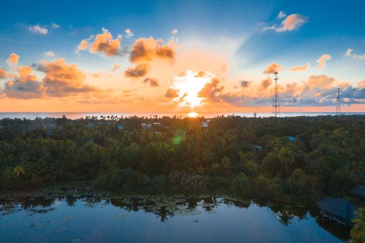 Drone shot capturing a breathtaking sunset over a tropical forest and calm water.
