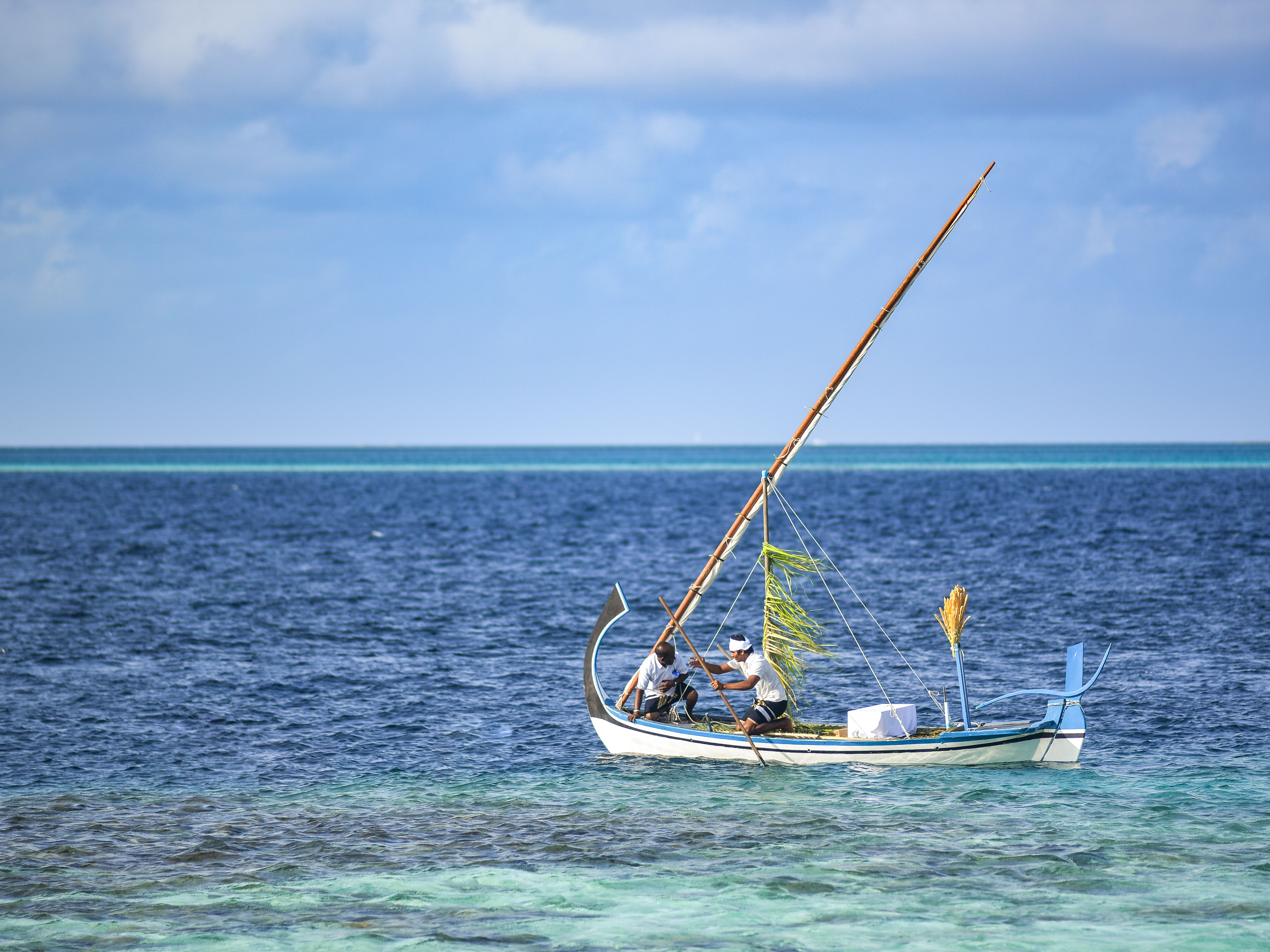 Two men sailing a traditional fishing boat on tranquil turquoise sea under a clear sky.