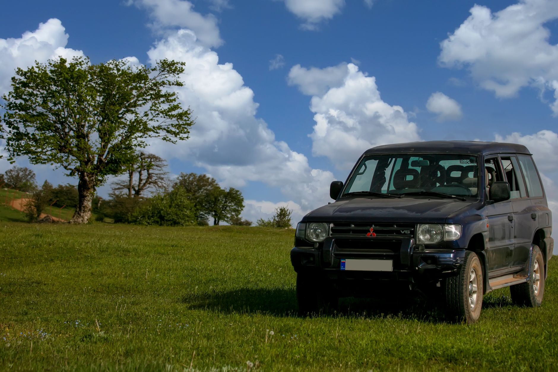 Mitsubishi SUV parked in green fields under a blue sky in Shahrud, Iran.