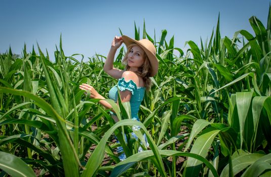 Caucasian woman in a sun hat amidst a green cornfield on a sunny summer day.