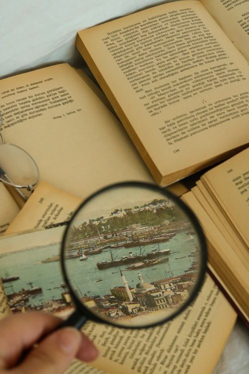 Free An artistic close-up of open vintage books with a magnifying glass highlighting a historical map. Stock Photo