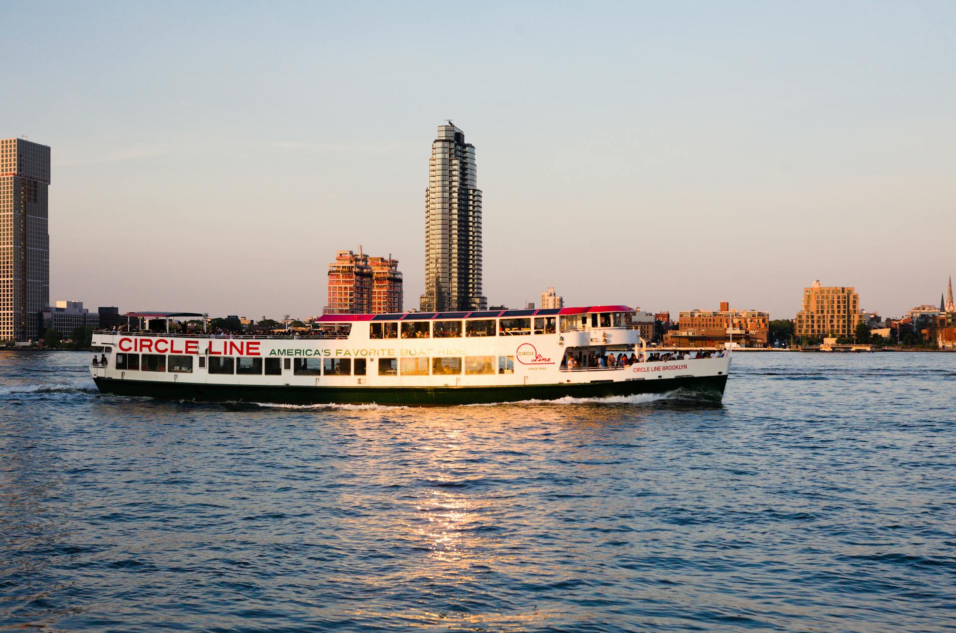 Circle Line ferry cruising in front of New York City skyline during sunset.