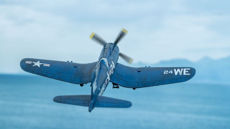 Historic Vought F4U Corsair airplane in flight over ocean, seen from behind.