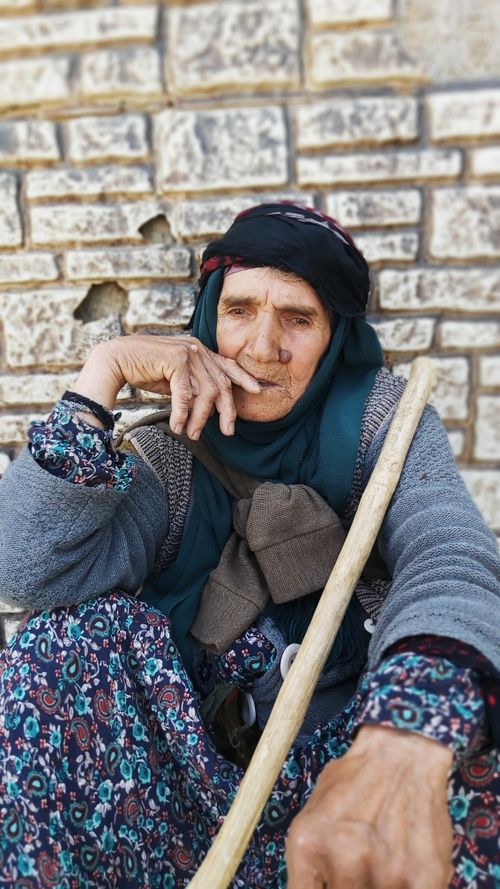 Free Senior woman in traditional clothing sits thoughtfully against a textured brick wall. Stock Photo