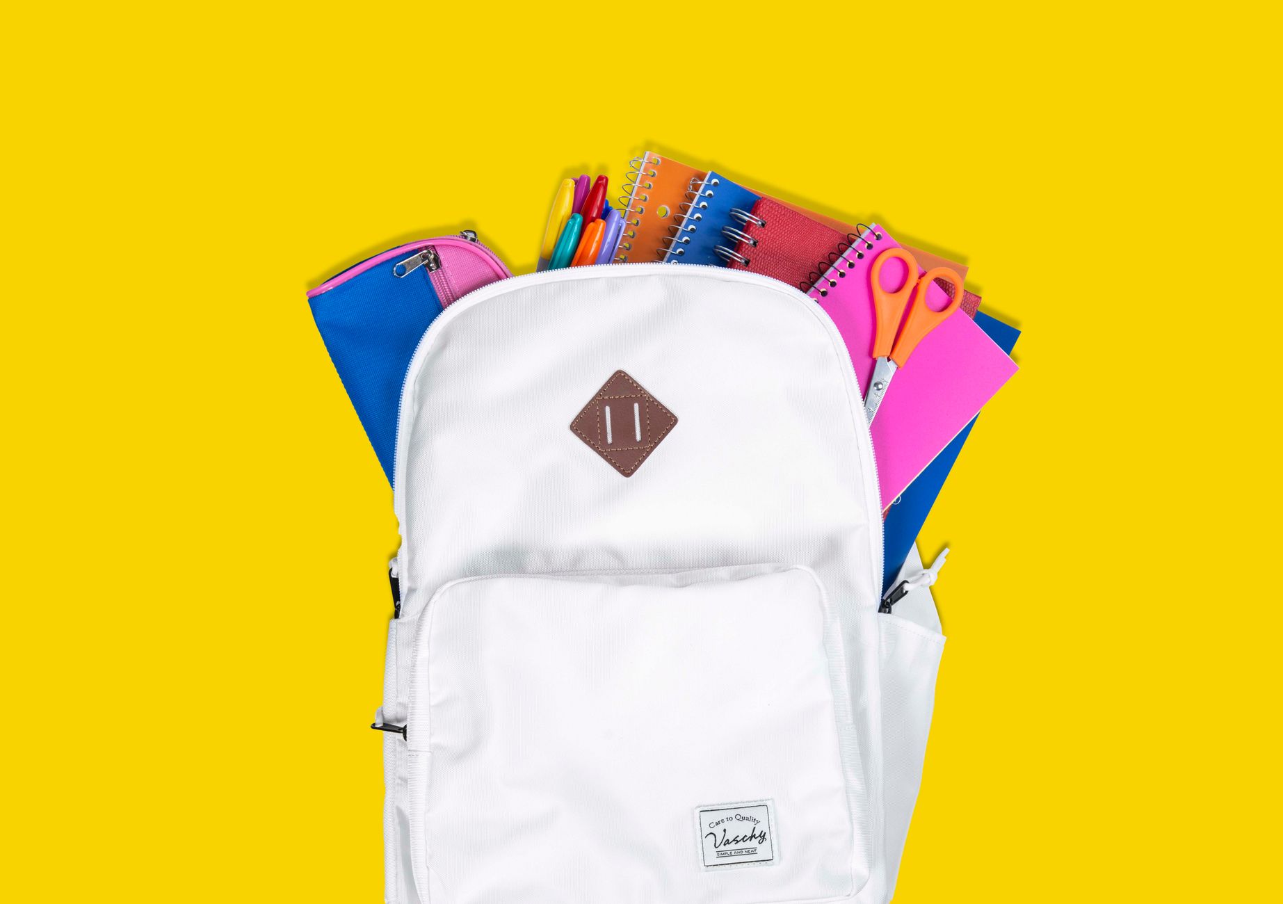 White backpack packed with colorful school supplies against a yellow background.