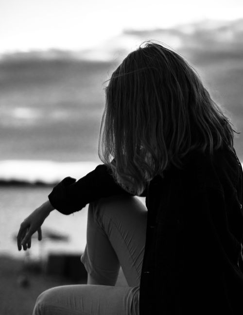 Free Black and white portrait of a woman in deep thought, sitting by the shore at dawn. Stock Photo
