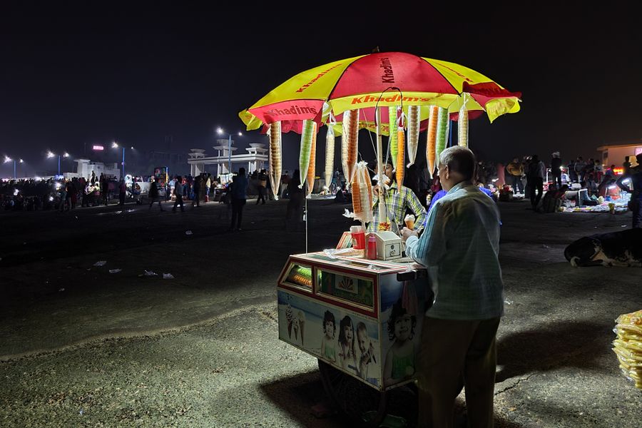 A street vendor sells ice cream cones at night in Digha, India, under a vibrant umbrella.