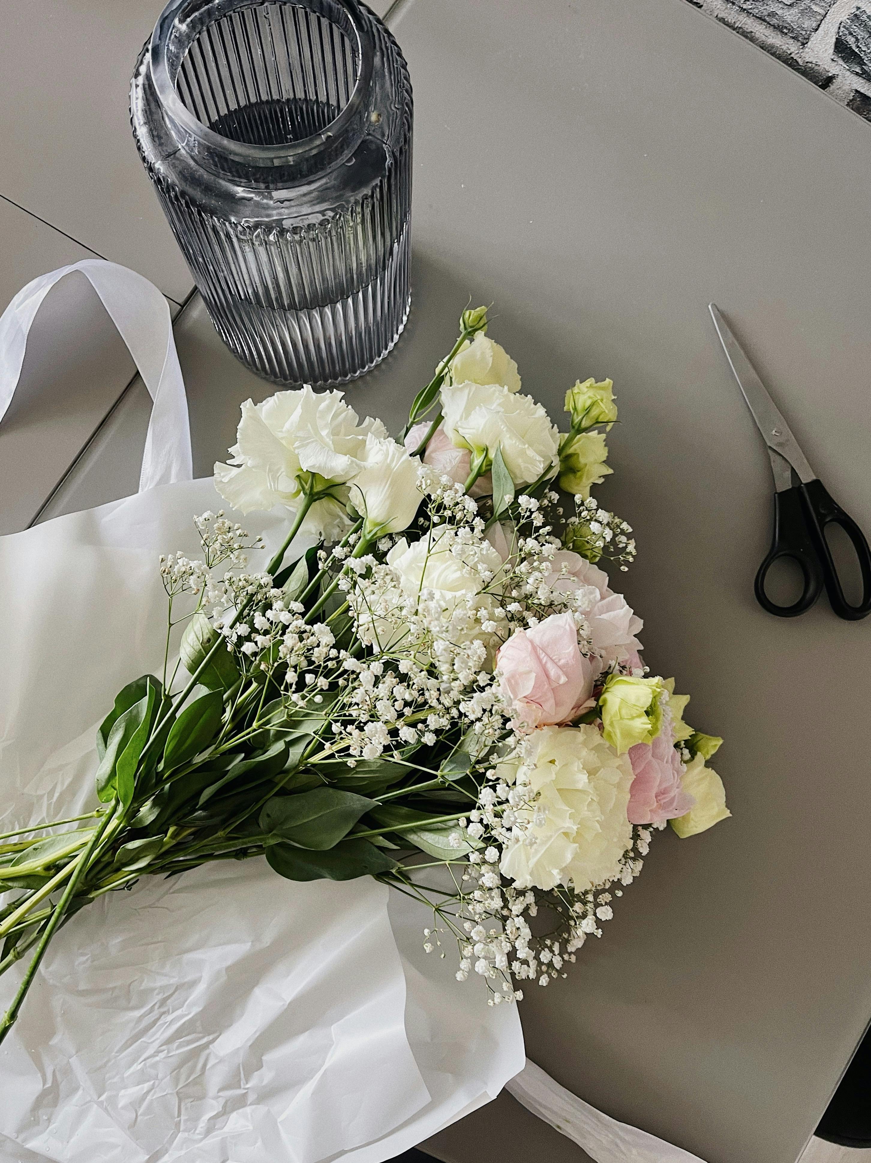A delicate bouquet of white and pink flowers with a vase on a table.