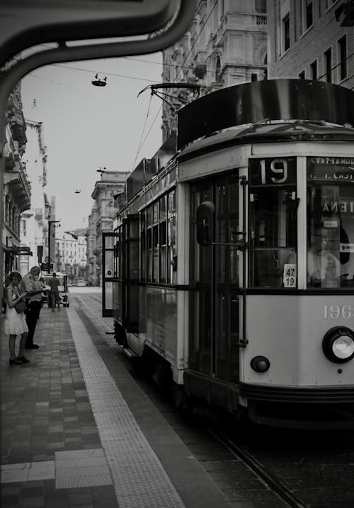 A Grayscale Photo of People Standing on the Street Near the Tram