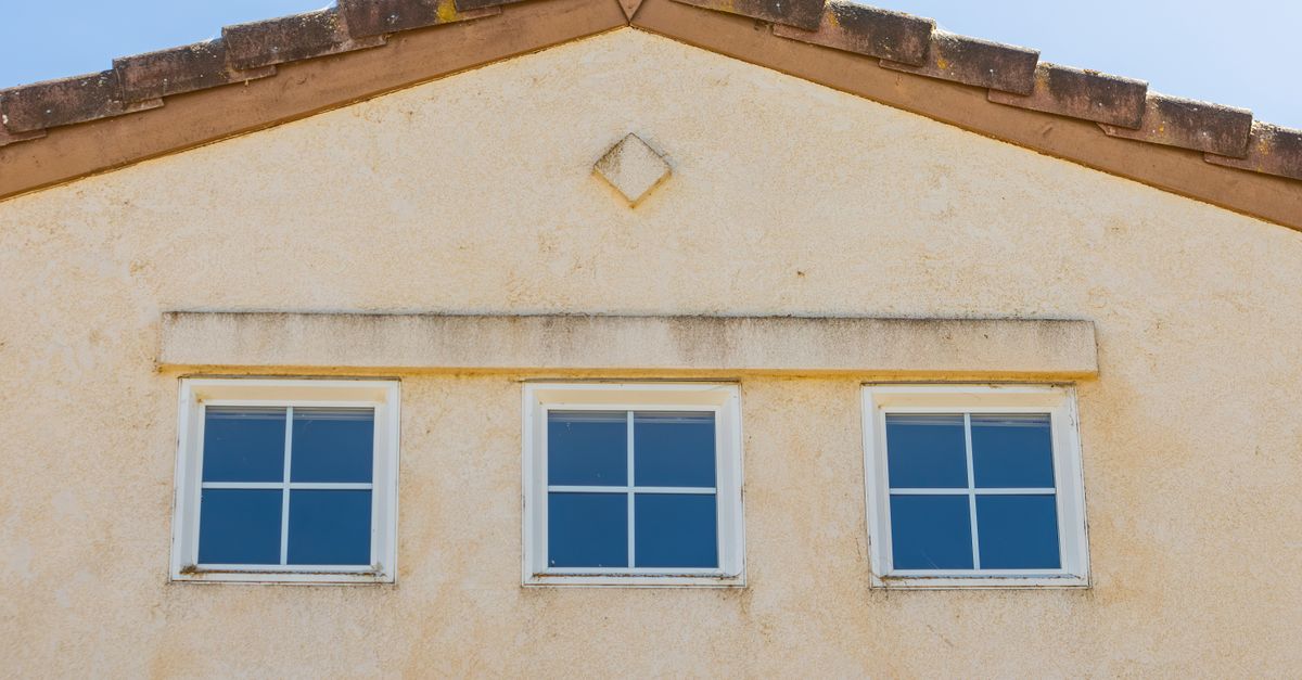 Close-up view of a house facade featuring three evenly spaced glass windows under a triangular roof.