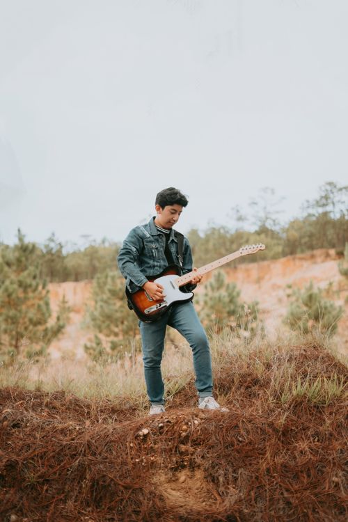 Free Adult male playing electric guitar in a field, showcasing musical passion in nature. Stock Photo