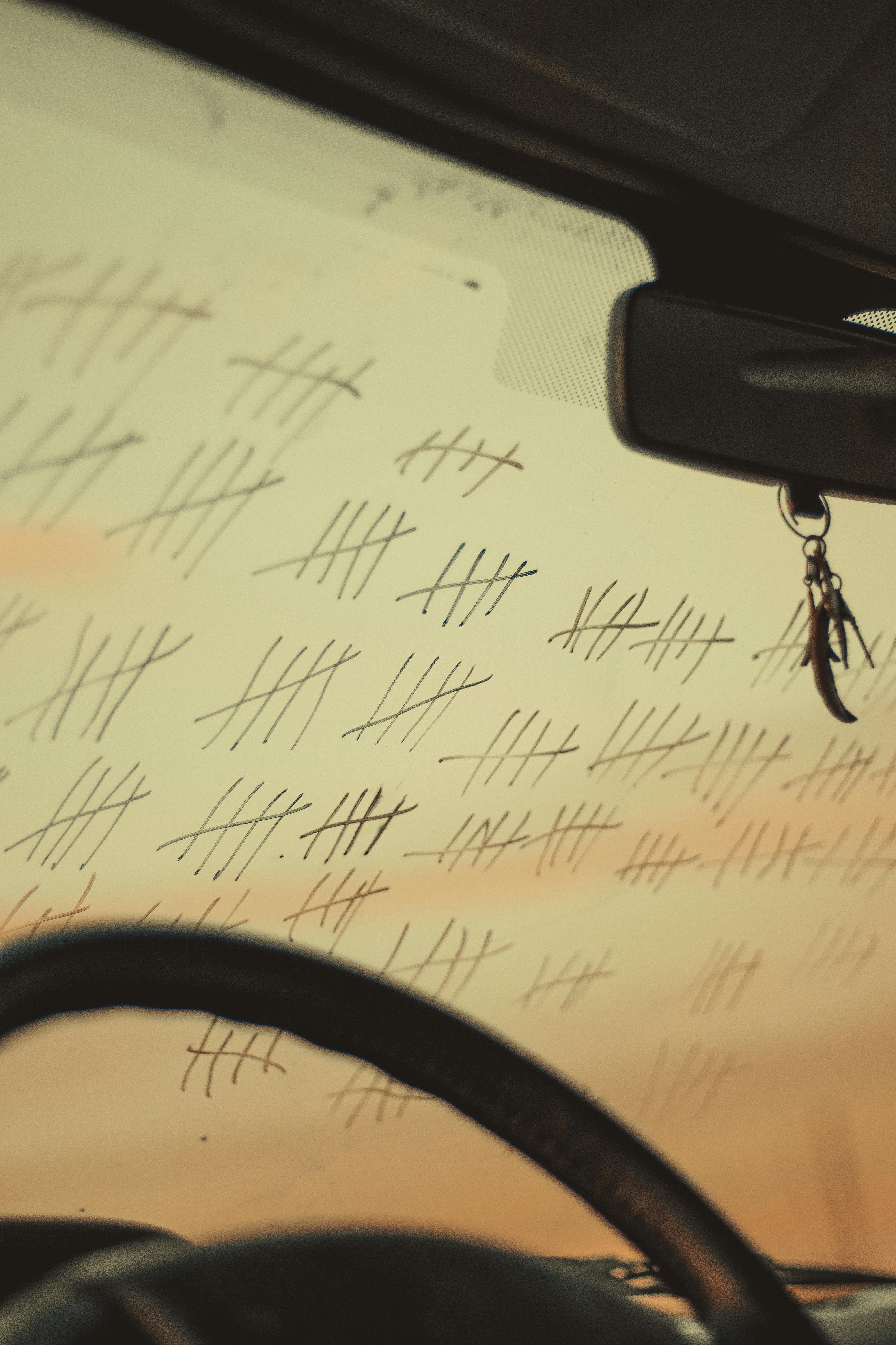 A car windshield filled with tally marks reflecting the sunset's orange glow.