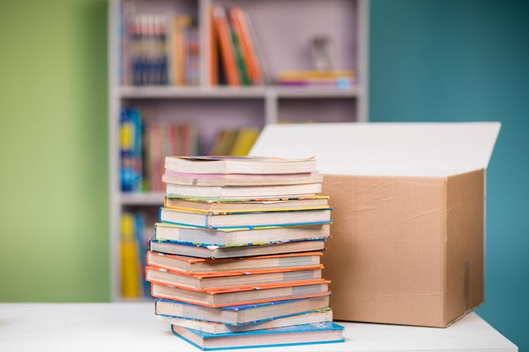 Close-up Photo Of Stacked Books Beside A Carton Box 