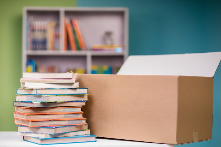 Close-up Photo Of Stacked Books Beside A Carton Box