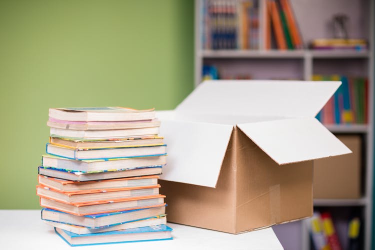 Close-up Photo Of Stacked Books Beside An Opened Carton Box 