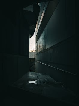 A dark, narrow urban passageway capturing the essence of modern architecture in low light.
