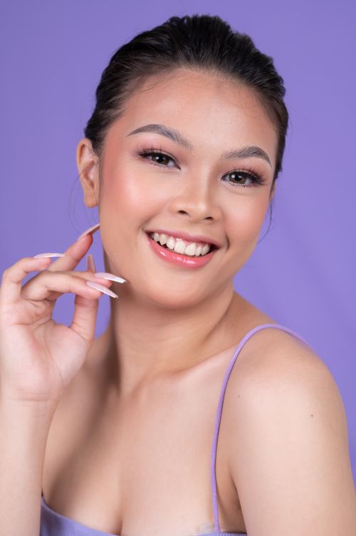Free Portrait of a smiling woman in a purple top against a purple background. Stock Photo