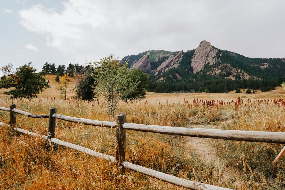 Scenic view of mountains and grassy field framed by a wooden fence in daylight.