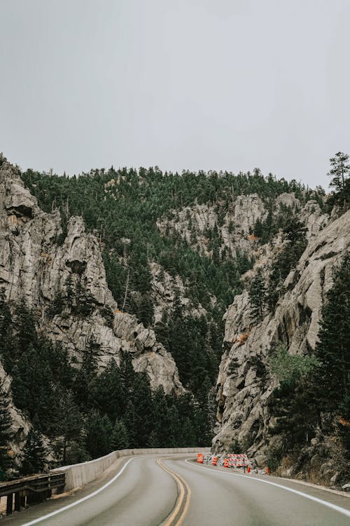 Asphalt Road Between Rocky Mountains with Green Trees