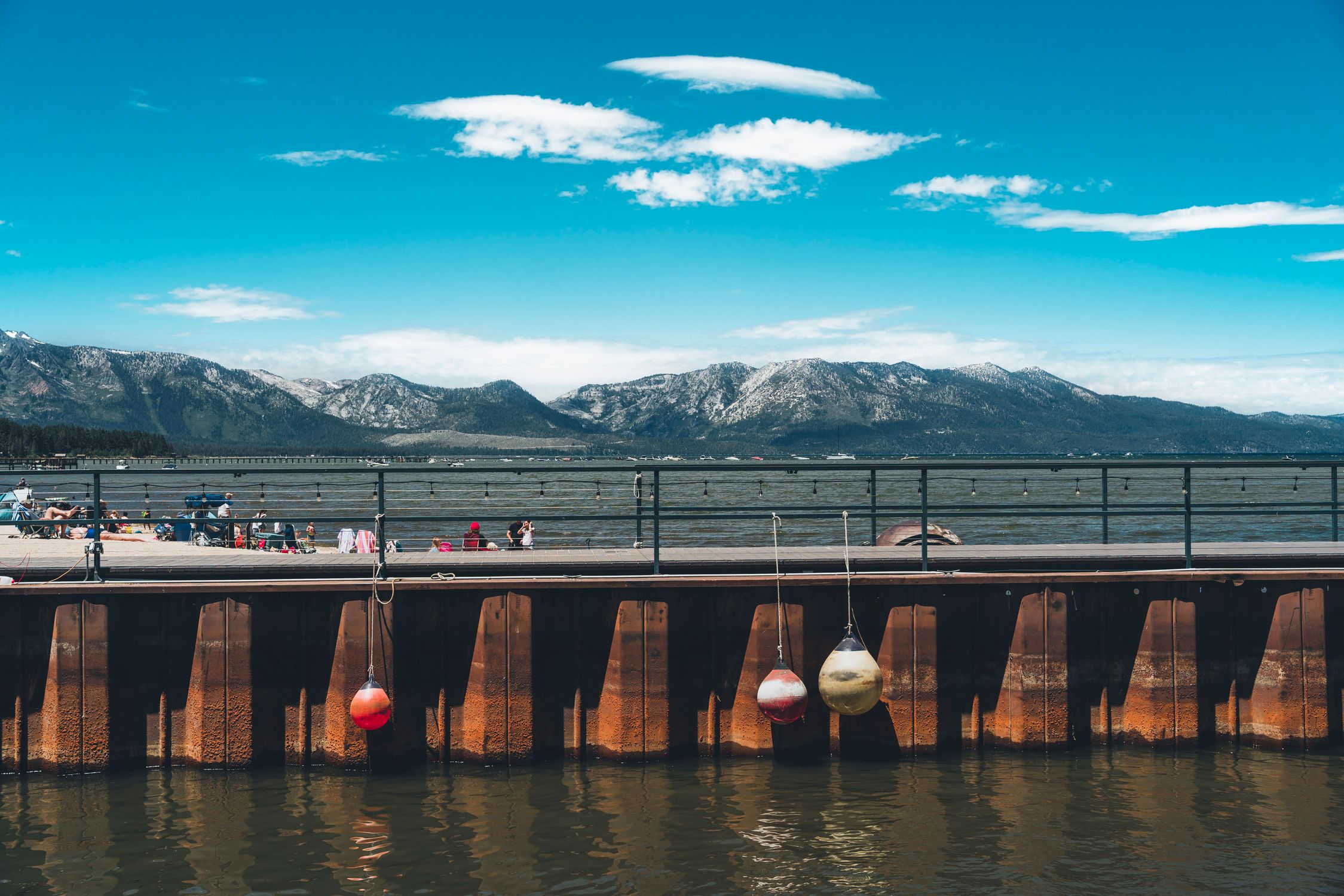 Enjoy a sunny day at Lake Tahoe with mountains and a bustling boardwalk.