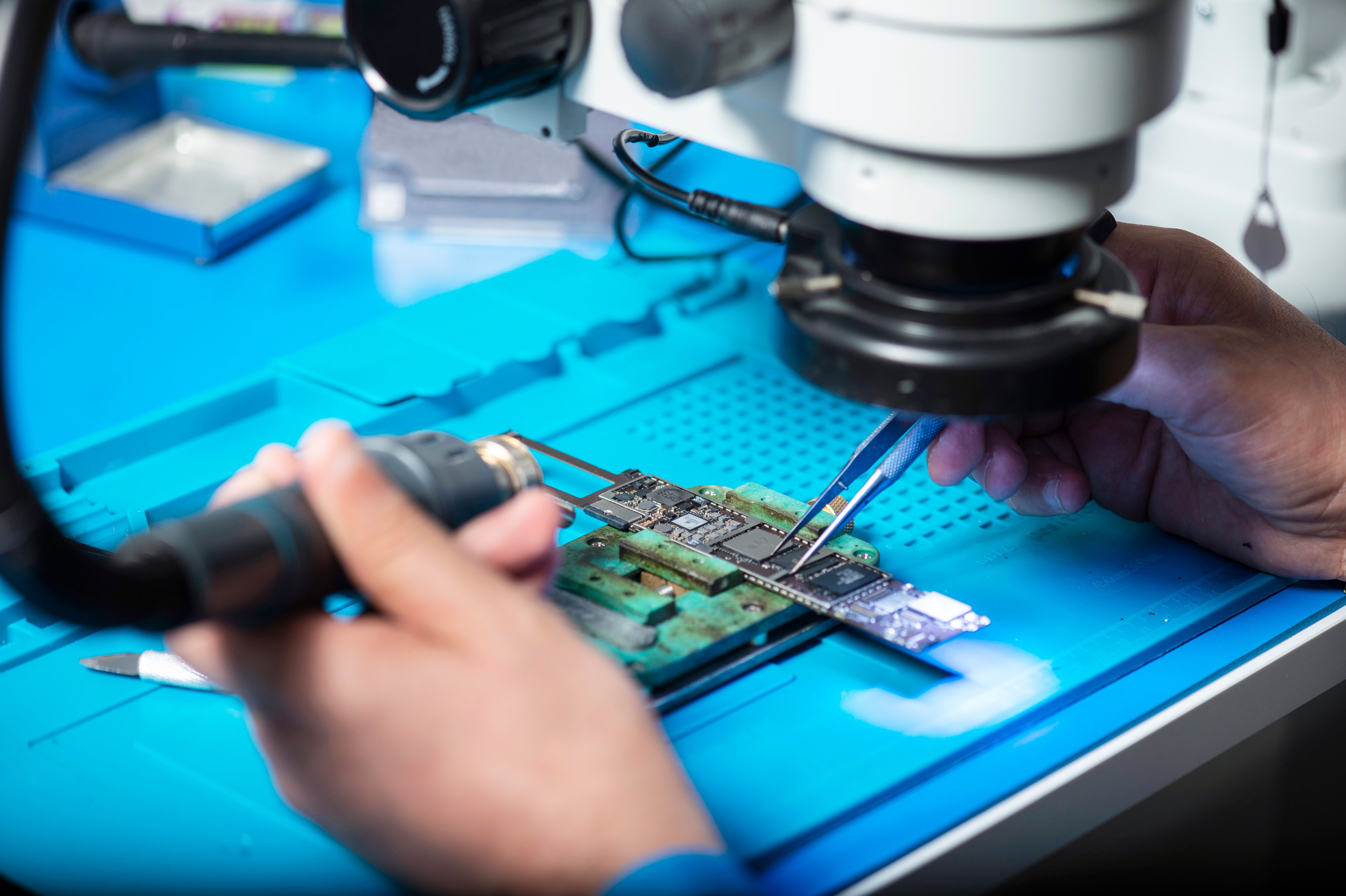 Técnico reparando una placa electrónica bajo microscopio