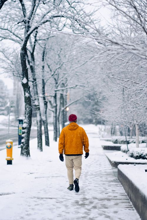 Free A person wearing a yellow jacket walks down a snow-covered sidewalk in Toronto. Stock Photo