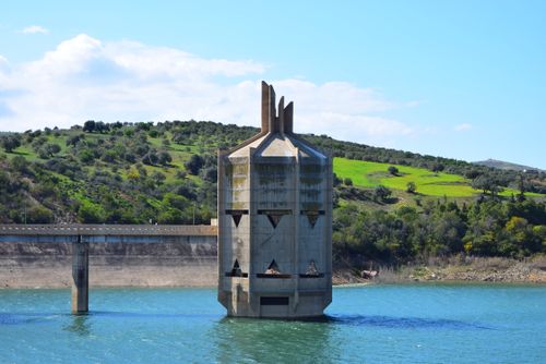 Free Concrete tower in Sidi Salem Dam, Tunisia, amid lush green hills and water. Stock Photo