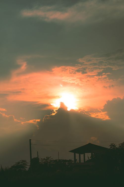 Free Silhouette of a house beneath a dramatic sunset sky with glowing orange and golden hues. Stock Photo
