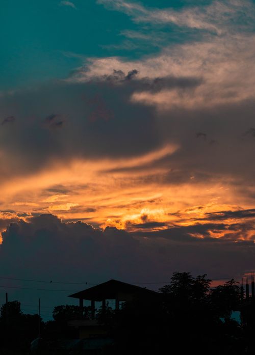 Free Dramatic sunset over silhouetted trees and houses under a vibrant sky. Stock Photo