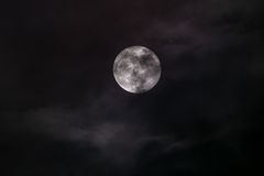An atmospheric shot of a full moon veiled by dark clouds, capturing the essence of nighttime.