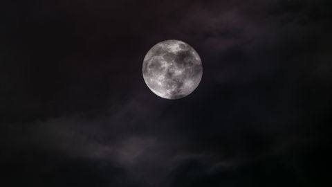 An atmospheric shot of a full moon veiled by dark clouds, capturing the essence of nighttime.