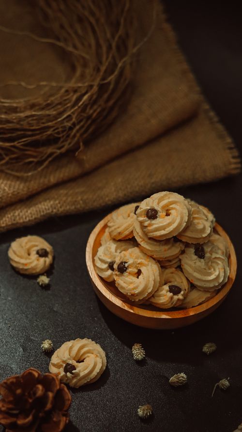 Free A bowl of cookies on a dark surface, surrounded by pinecones and rustic elements. Stock Photo
