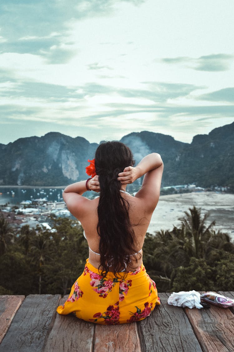 Back View Shot Of A Woman Sitting On A Wooden Dock While Looking At The Beautiful Scenery