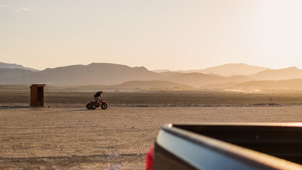 Silhouette of a person riding an ATV in a desert landscape during sunset.