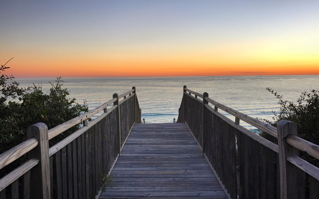 Peaceful sunset over the ocean from a wooden boardwalk at Alys Beach, Florida, offering a serene coastal escape.