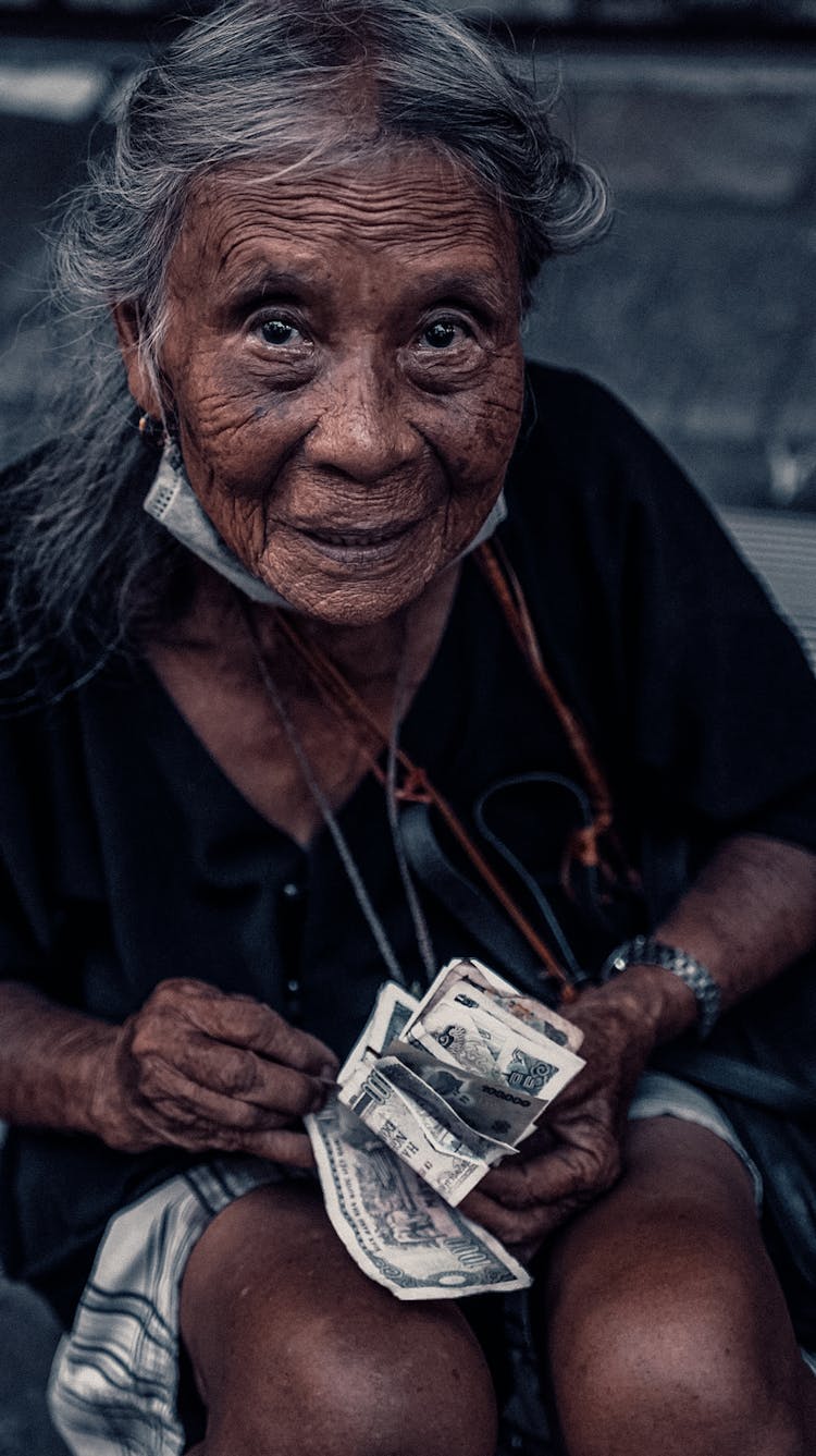 An Elderly Woman In Black Shirt Holding A Paper Money