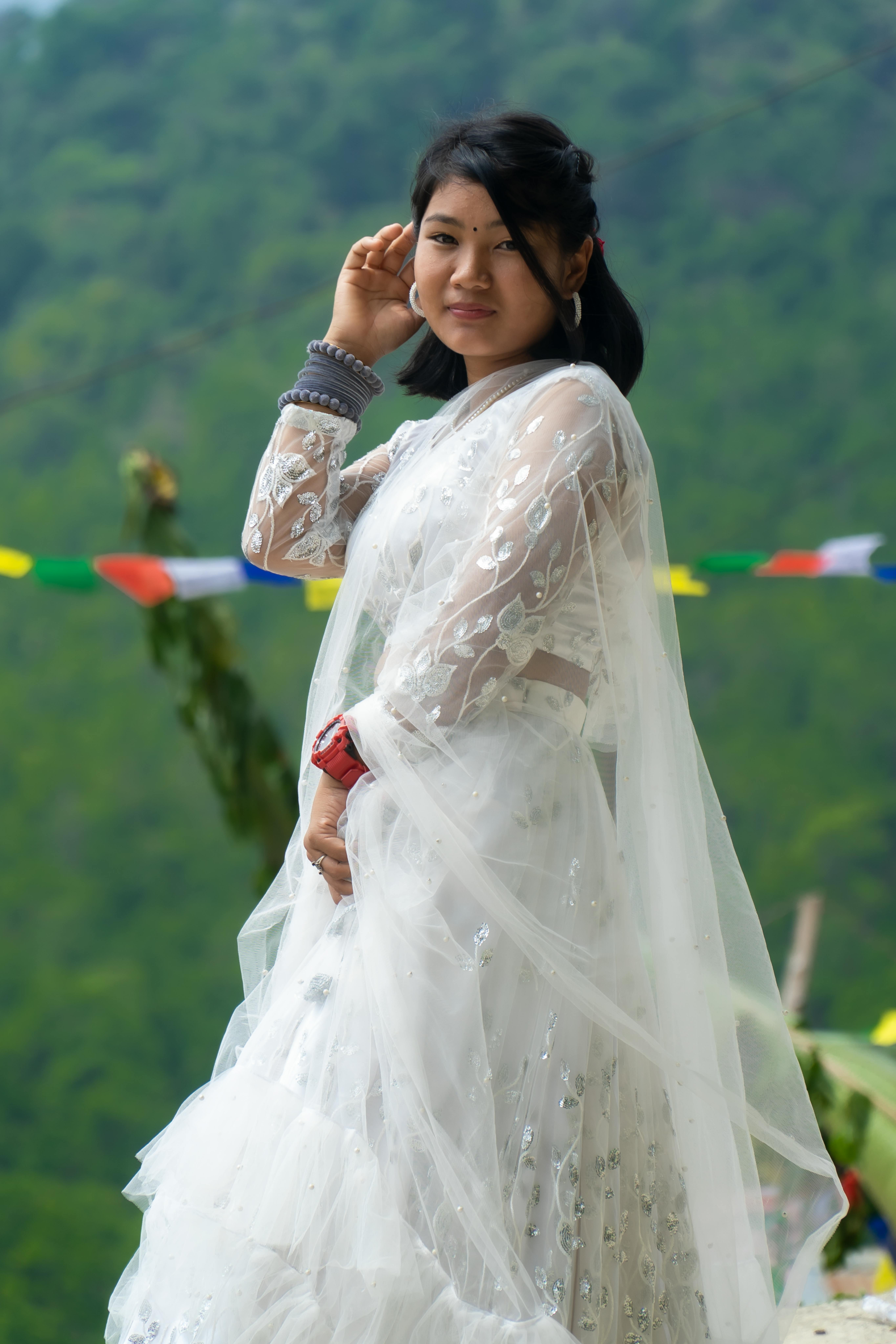 A beautiful Asian woman poses outdoors in a white bridal gown with vibrant flags in the background.