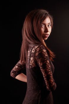Side view portrait of young brunette woman in a lace dress against dark backdrop.