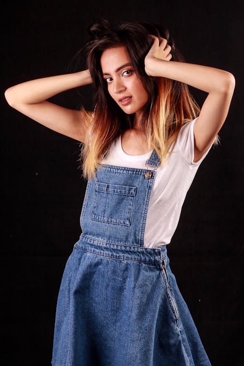 Woman in Denim Jumper Touching Her Hair while Posing at the Camera