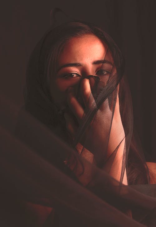 Woman in Black Veil Covering Her Mouth while Looking at the Camera