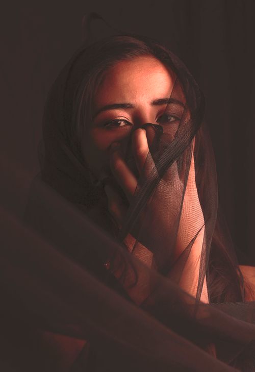 Free A dramatic portrait of a woman partially covered by a dark veil, evoking mystery and emotion. Stock Photo