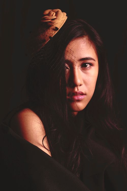 Free Close-up portrait of a young woman with elegant hat. Dramatic lighting enhances her expression. Stock Photo