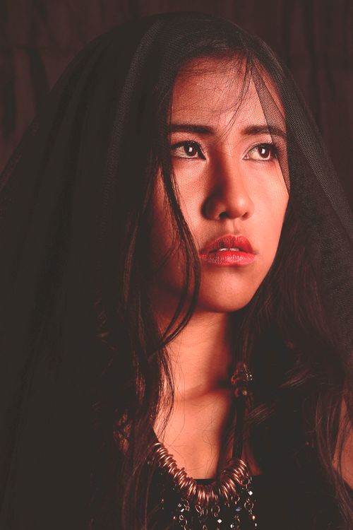Free Striking portrait of a woman looking afar, draped in a veil against a black background. Stock Photo