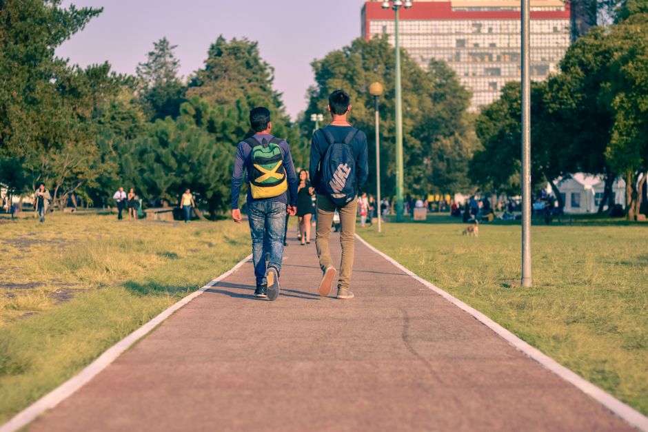 Dos personas caminando por un camino pavimentado en un parque verde en Ciudad de México.